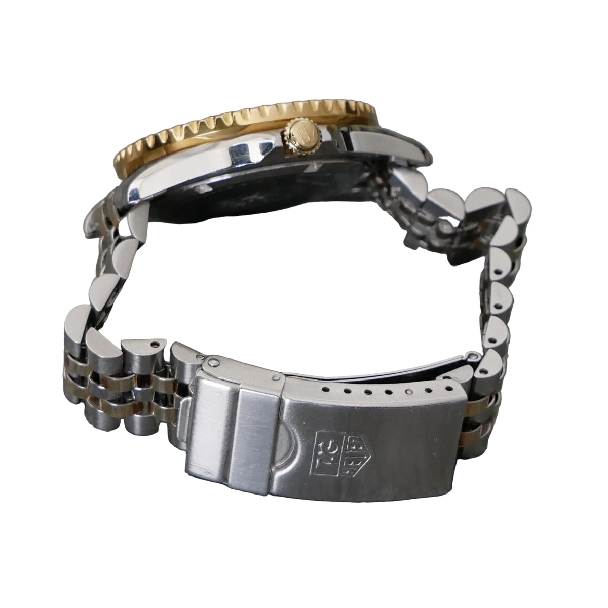 Close-up of a watch with a gold crown and silver metal band on a gray background