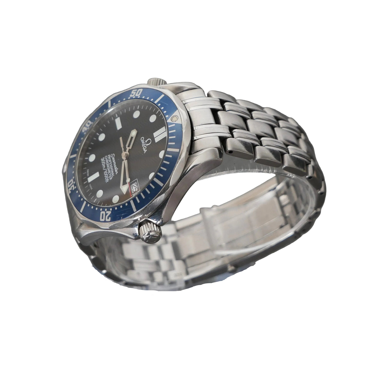 A stainless steel wristwatch with a silver-tone metal bracelet and a dark gray dial, featuring a blue bezel with white markings. The watch is displayed on a clear acrylic stand against a dark gray textured background.