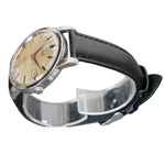 Vintage watch with black strap on a clear stand against a gray background