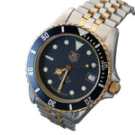 A two-tone stainless steel and gold Tag Heuer Submariner watch with a dark blue dial, blue bezel, and matching blue and gold link bracelet, shown on a white background.