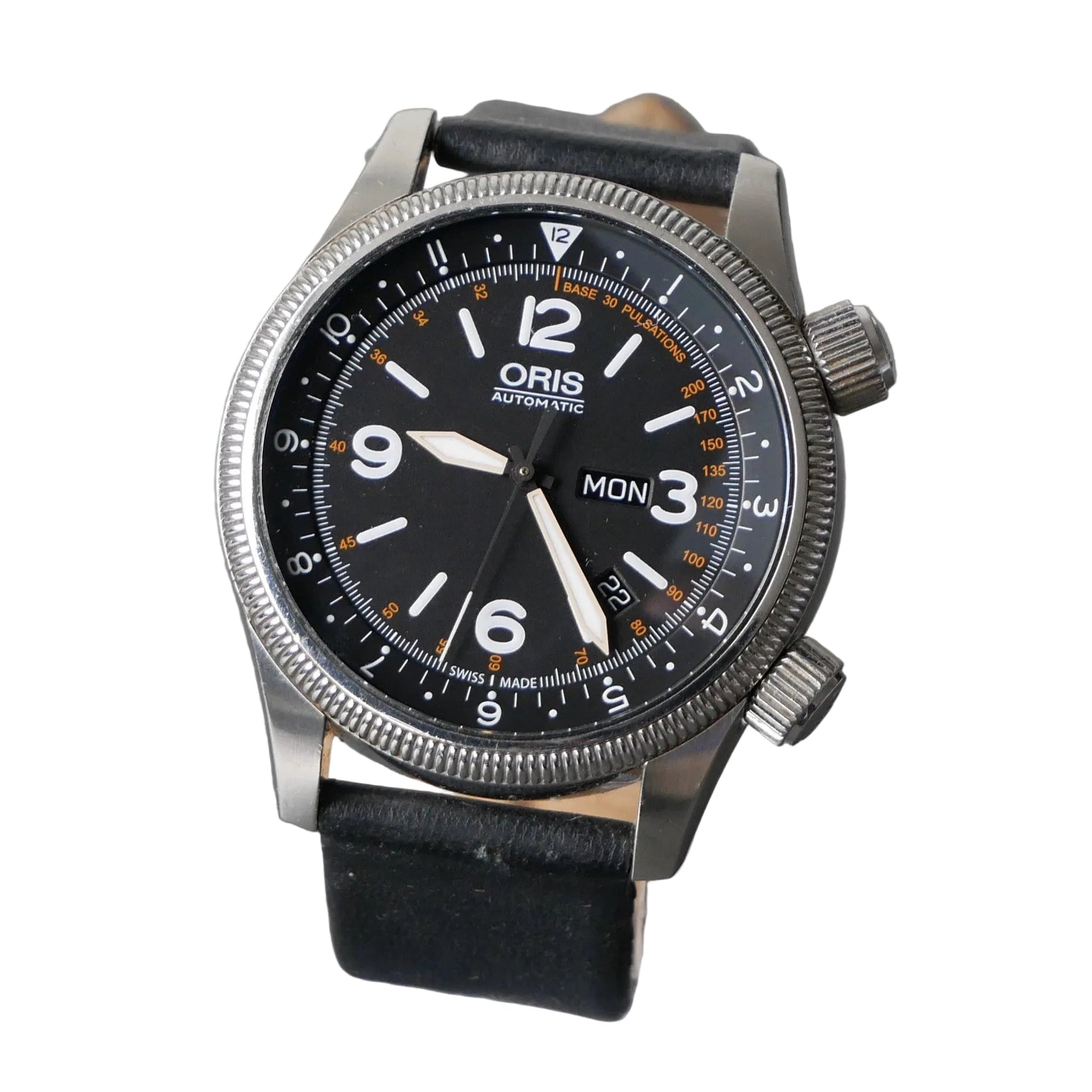 An Oris Automatic watch with a black dial, silver-tone stainless steel case, and a black leather strap, displayed on a clear stand against a textured gray background.